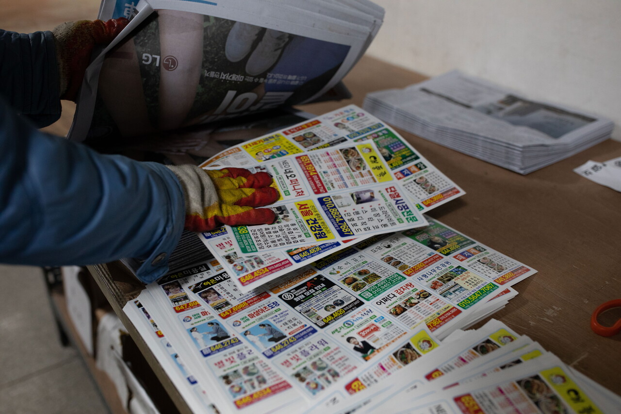 신문배달원이 신문에 ‘삽지’라고 불리는 광고 전단지를 넣고 있다. ⓒ 박시몬