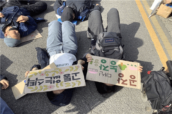  4.14 기후정의파업 참가자들이 ‘다이-인 액션’을 위해 도로 바닥에 누워있다. 공장식 축산에 항의하거나 후쿠시마 오염수 방류를 반대하는 내용의 손팻말도 보인다. 우현지 기자