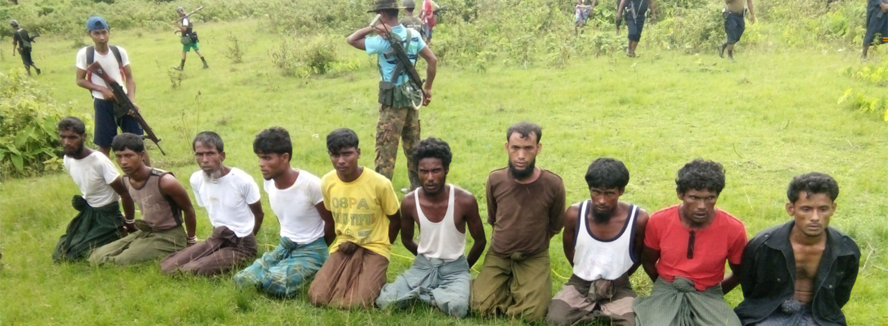 와론과 쵸소우가 확보한 사진 3장 중 1장. 10명의 로힝야족 남성들이 무릎을 꿇고 일렬로 앉아있다. 뒤에 있는 남성 2명은 미얀마 제8보안경찰대대 소속 경찰이다. 출처 로이터