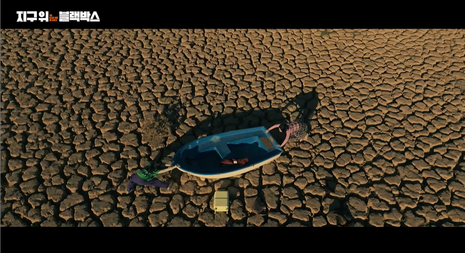 스페인 메마른 강바닥에서 모니카와 립제이가 작은 배를 중심에 놓고 춤을 추고 있다. 웨이브 지구 위 블랙박스 화면 갈무리