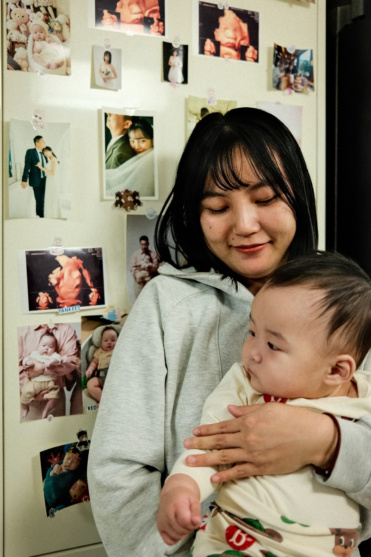 지난 1월 17일 김가윤(왼쪽)이 가족사진으로 꾸며진 벽 앞에서 7개월 된 아이를 안고 있다. 홍성민 기자