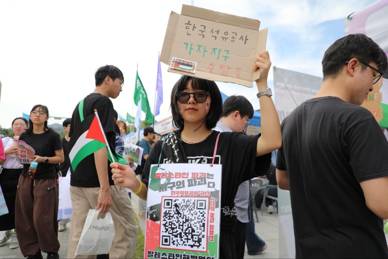 ‘팔레스타인과 연대하는 한국 시민사회 긴급행동’의 이서염 자원활동가가 팔레스타인 국기와 함께 ‘한국석유공사 가자지구 수탈 중’이라고 쓴 손팻말을 들고 있다. 한국석유공사 의 자회사인 영국 기업이 가자지구에서 이익을 취한다고 비판하는 내용이다. 이민기 기자